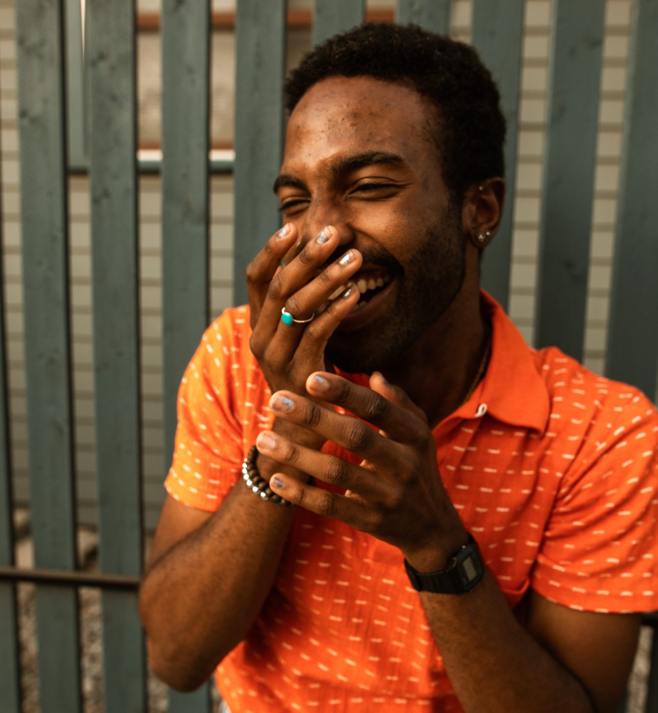 Man in Orange Shirt Laughing with Hands on Mouth