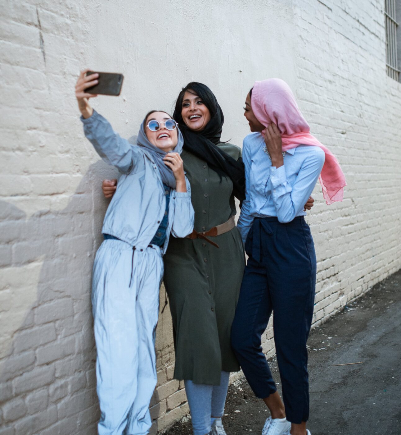 three women smiling whilst taking a picture on a mobile phone.