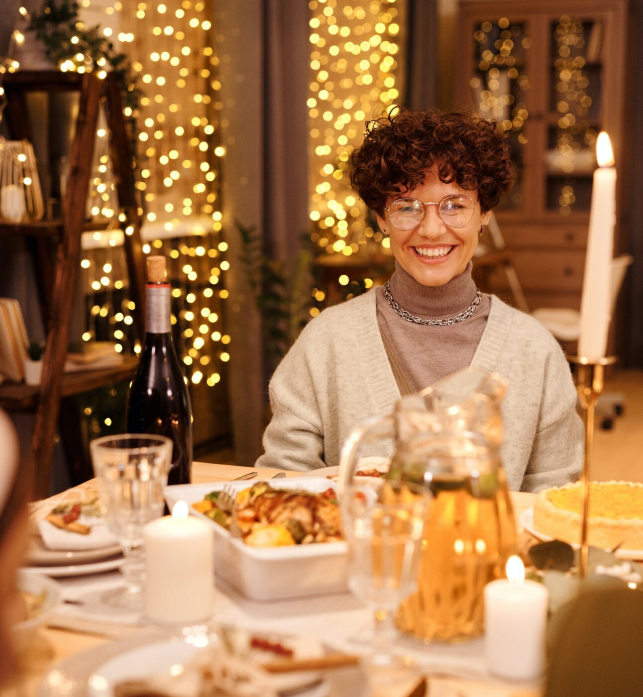 A person sat at a table surrounded by friends and Christmas lights.